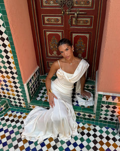 Elevate your elegance with the Celine Corset Gown, a luxurious satin masterpiece designed to flatter every figure. Featuring a corset waist that sculpts your silhouette and graceful draping at the hips, this gown enhances your natural curves. The asymmetric design highlights a delicate rosette on one shoulder and a flowing scarf on the other, adding a unique touch of sophistication. The slightly flared hemline completes this stunning look, perfect for making a memorable entrance at any special occasion.