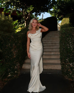 Elevate your elegance with the Celine Corset Gown, a luxurious satin masterpiece designed to flatter every figure. Featuring a corset waist that sculpts your silhouette and graceful draping at the hips, this gown enhances your natural curves. The asymmetric design highlights a delicate rosette on one shoulder and a flowing scarf on the other, adding a unique touch of sophistication. The slightly flared hemline completes this stunning look, perfect for making a memorable entrance at any special occasion.
