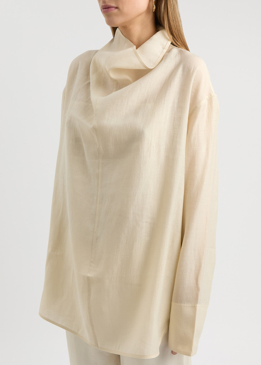 Elevate your wardrobe with this draped woven blouse by Toteme featuring a sophisticated funnel neck and relaxed dropped shoulders for effortless style. The curved hem with a longer back adds a contemporary silhouette, while the detachable cami lining offers versatility and comfort. Perfect for both casual and polished looks, this blouse combines elegance with adaptable wearability.