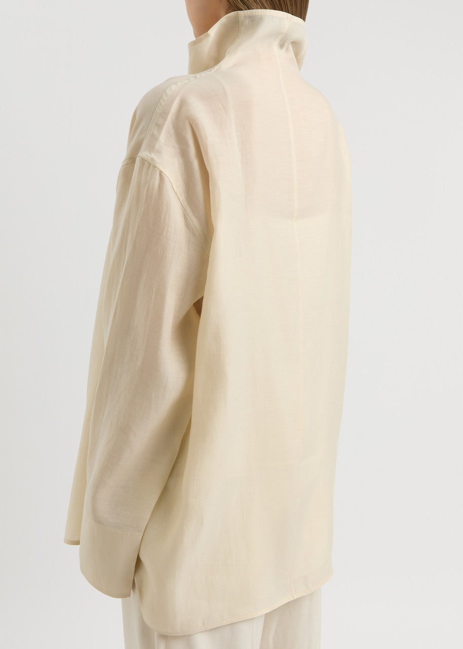 Elevate your wardrobe with this draped woven blouse by Toteme featuring a sophisticated funnel neck and relaxed dropped shoulders for effortless style. The curved hem with a longer back adds a contemporary silhouette, while the detachable cami lining offers versatility and comfort. Perfect for both casual and polished looks, this blouse combines elegance with adaptable wearability.