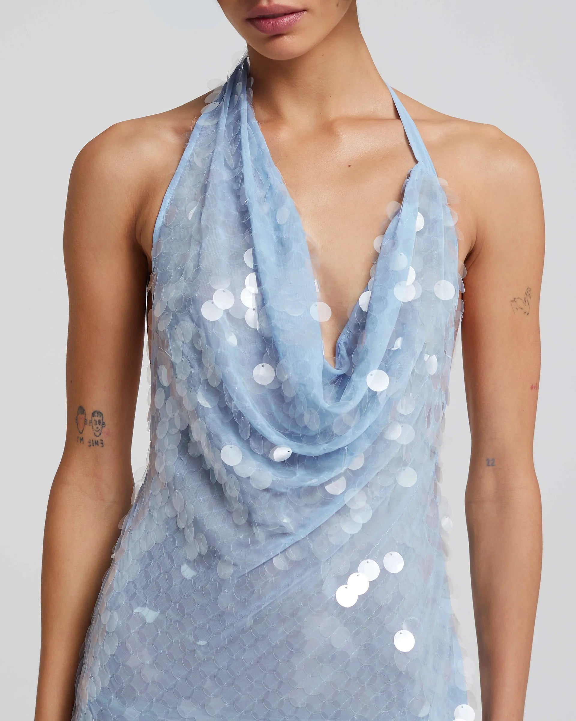 Expertly crafted with a bias cut, the Anais Dress elegantly drapes the body, shimmering and glistening in a sea of cornflower blue paillettes. Its adjustable cowl neckline and waist tie ensure a perfect fit, making it a must-have for any occasion.