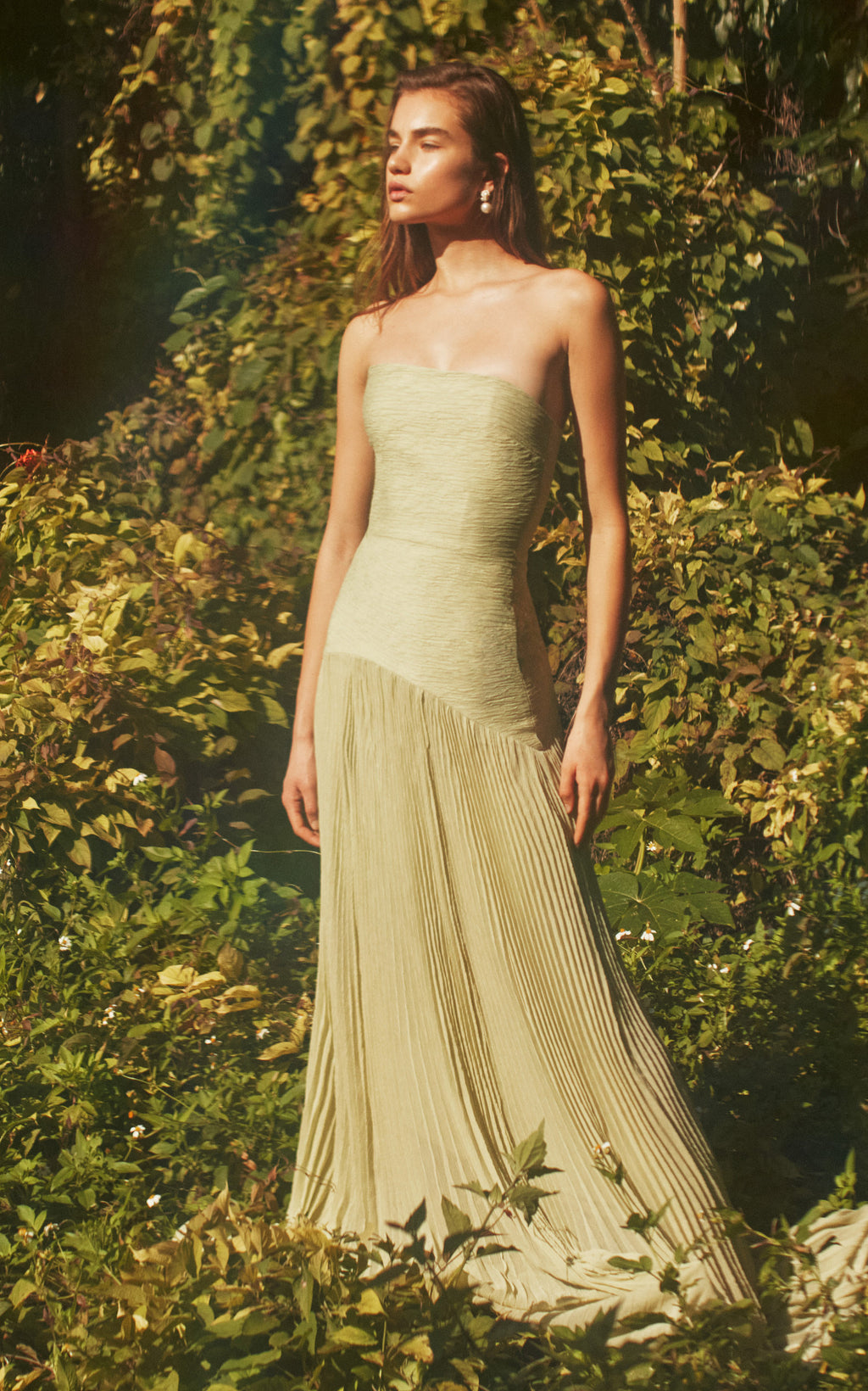 The Sunniva Plisse Strapless Gown showcases a fitted strapless bodice with a gracefully curved dropped waist, leading into a flowing plisse skirt that moves elegantly with every step. Its timeless silhouette emphasizes a refined, feminine shape, perfect for occasions that call for understated sophistication. Pair with statement earrings to elevate the look, capturing the essence of modern elegance.