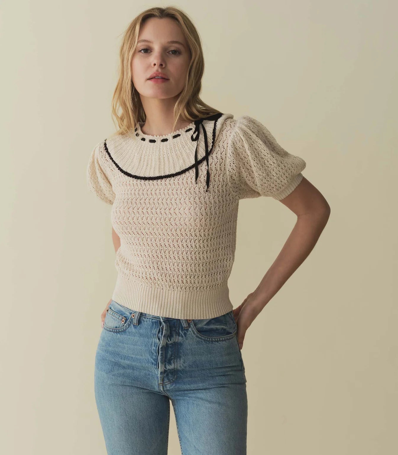 Crafted from 100% Pima cotton, the Glenda Sweater features a cropped silhouette and a ‘40s-inspired collar decorated with a contrast black grosgrain ribbon and scalloped trim. Ribbing lends texture to the cuffs and hem, while light shirring at the shoulders adds a bit of volume.