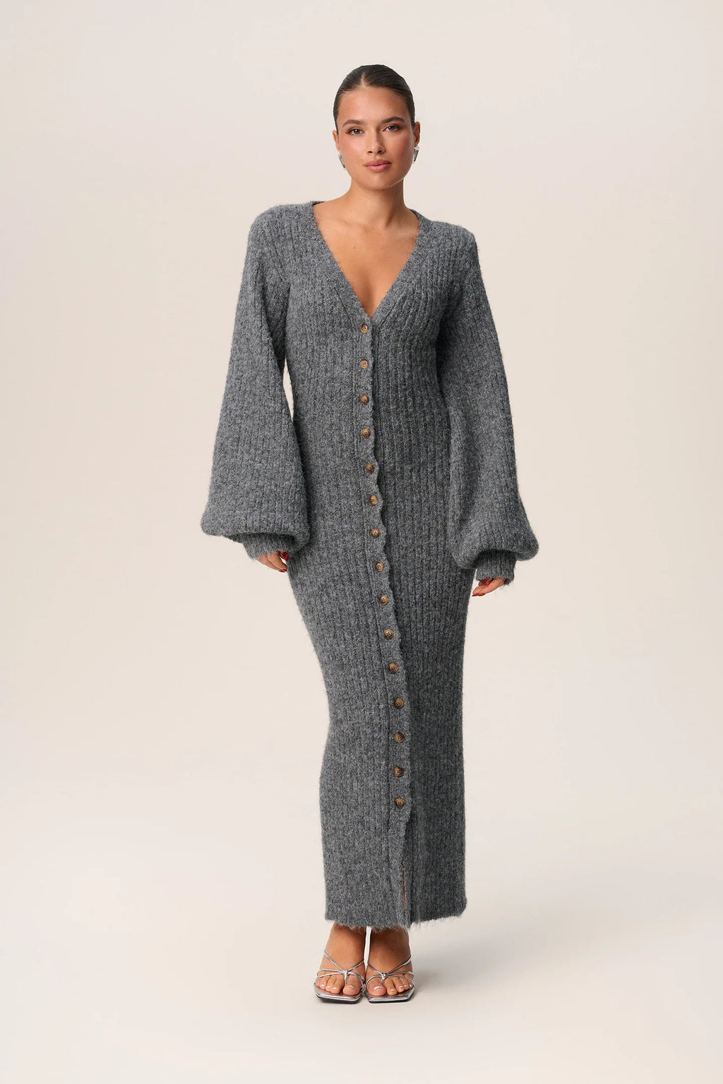 Indulge in luxury with the Luzern Knit Dress. This maxi dress in grey melange is expertly crafted from a soft and cozy wool-blended fabric, ensuring both style and warmth. It features a flattering hourglass fit, front button-up closure, and elegant V-neck collar. Complete the look with full-length balloon sleeves and distinctive cuffs for a truly sophisticated and exclusive feel.