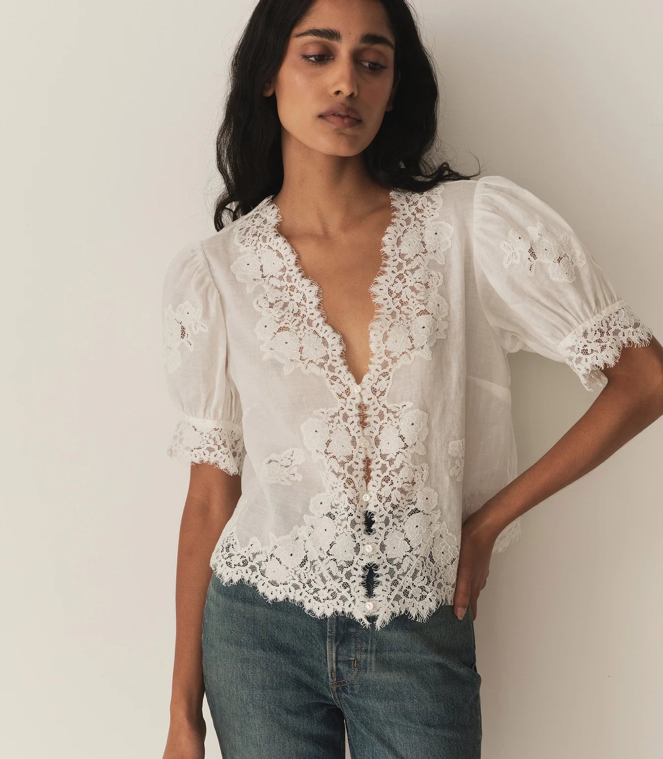 Crafted from lightweight, crisp ramie, the Idella Top from Doen features a plunging V-neckline, short puffed sleeves, and intricate embroidered lace details. Mother-of-pearl buttons adorn the front, while lace insets add delicate touches. This antique-inspired top is perfect for a breezy, feminine look.