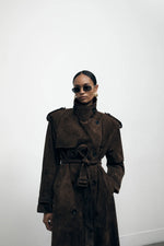 Load image into Gallery viewer, Elevate your wardrobe with the Brown Suede Trench Coat from Desavary London. Crafted with luxurious suede, this double breasted coat boasts an oversized fit and structured shoulders for a look that exudes sophistication. The buckle waist belt and storm flap add practicality to this statement piece. A must-have for any fashion-forward individual.
