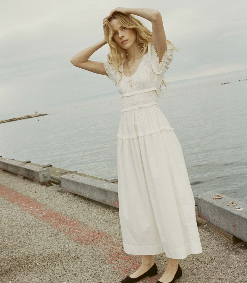 Crafted from crisp organic cotton poplin, the Leanne Dress features a scoop neckline, a gathered bust, and a fitted bodice framed with petite ruffles. A third gathered panel finishes just below the hips, flaring out into an ankle-length skirt, while elastic lends give to the short puffed sleeves, bust, and waist.