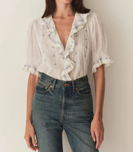 Introducing the luxurious Hettie Top. Made from the softest organic cotton voile for ultimate comfort. The Edwardian-inspired design features a plunging V-neckline and lace-trimmed ruffles, with embroidered daisies, pintuck details, and hidden starburst buttons. Perfect for tucking into your favorite high-waisted jeans or wearing loose for a relaxed yet elegant look.