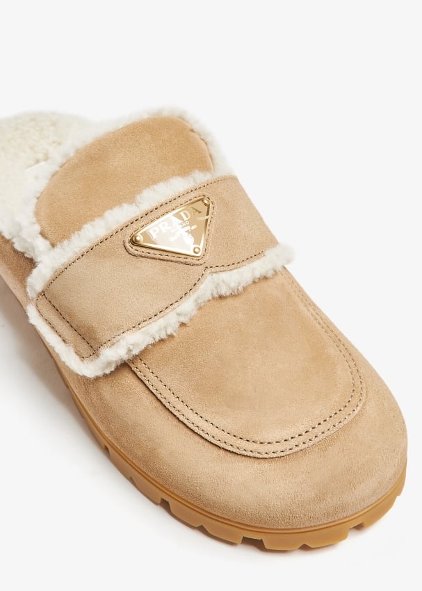 Embrace luxury and comfort with Prada's Shearling-lined suede mules. The soft shearling lining and chunky rubber sole provide a cozy feel and sturdy grip, while the enameled metal logo adds a touch of sophistication. Perfect for the risk-taker who values both style and comfort!