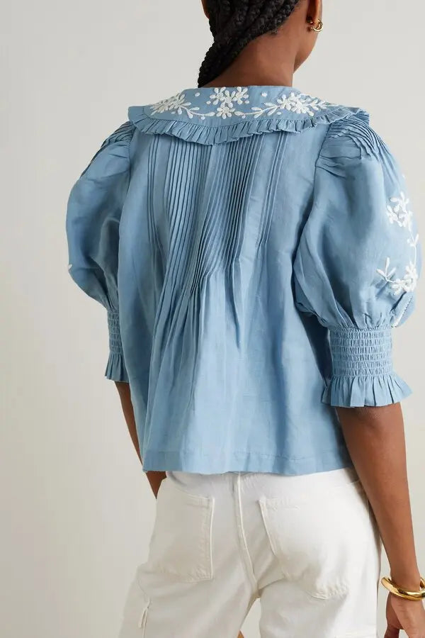 Introducing the Kyla Embroidered Cotton Blouse by Sea. This vintage-inspired blouse will add an air of sophistication to your wardrobe. Made with a breathable cotton and linen blend, it features delicate floral embroidery, ruffled collar, and pintucked details. Transform your look with this charming and unique piece.