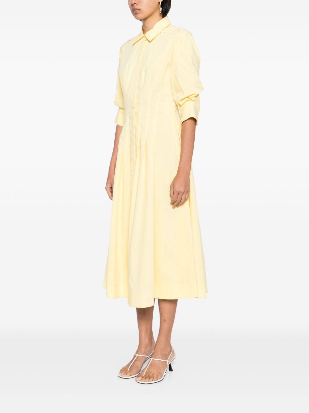 Introducing the Simkhai Jazz Midi Dress in a striking sulfur yellow. Made with a comfortable cotton blend, this dress features pintuck detailing and a straight-point collar. The three-quarter length puff sleeves and flared skirt add a touch of femininity. With a concealed front button fastening, buttoned-cuff sleeves, and two side inset pockets, this dress is both functional and stylish. Complete with full lining and a midi-length straight hem, this dress is perfect for any occasion.