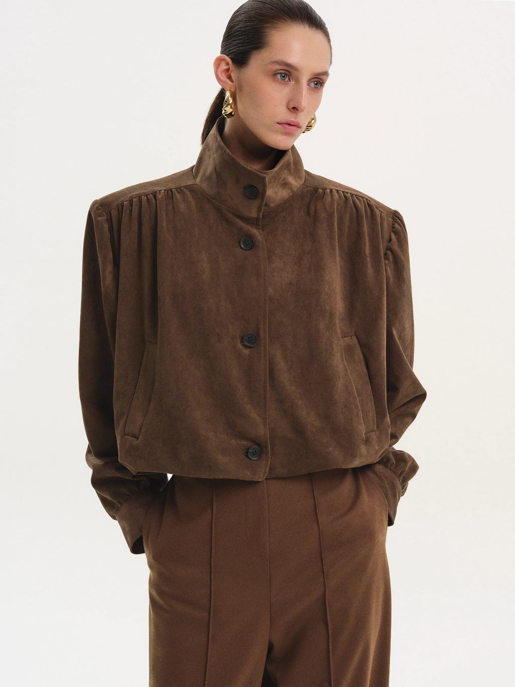 This ruched suede bomber jacket combines classic style with modern details. Its boxy shape and padded shoulders give a confident edge, while the stand collar and gathered pleats add subtle sophistication. The softly structured waistband offers a gentle blouson effect, creating a relaxed yet polished silhouette. Fully lined for comfort, this jacket is perfect for elevating any outfit with effortless charm.