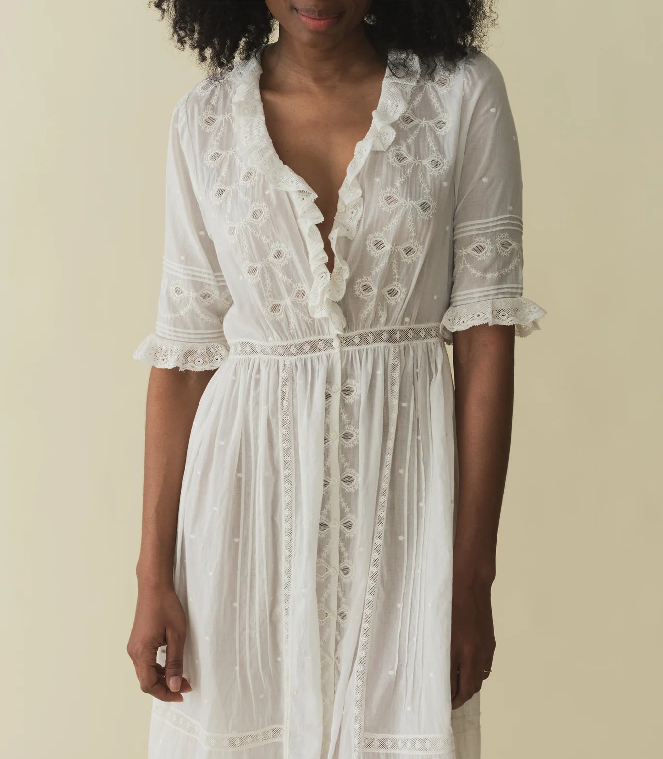 Crafted from the softest organic cotton voile, the Victorian-inspired Rosabella Dress features a plunging V-neckline framed with cascading scalloped lace-trimmed ruffles that extend down the bodice. Alternating panels of inset lace, clustered pintucks, and intricate bow embroidery adorn the front, back, and elbow-length sleeves. A line of hand-crocheted buttons run down the front, while inset lace decorates a fitted waist and ankle-grazing skirt.