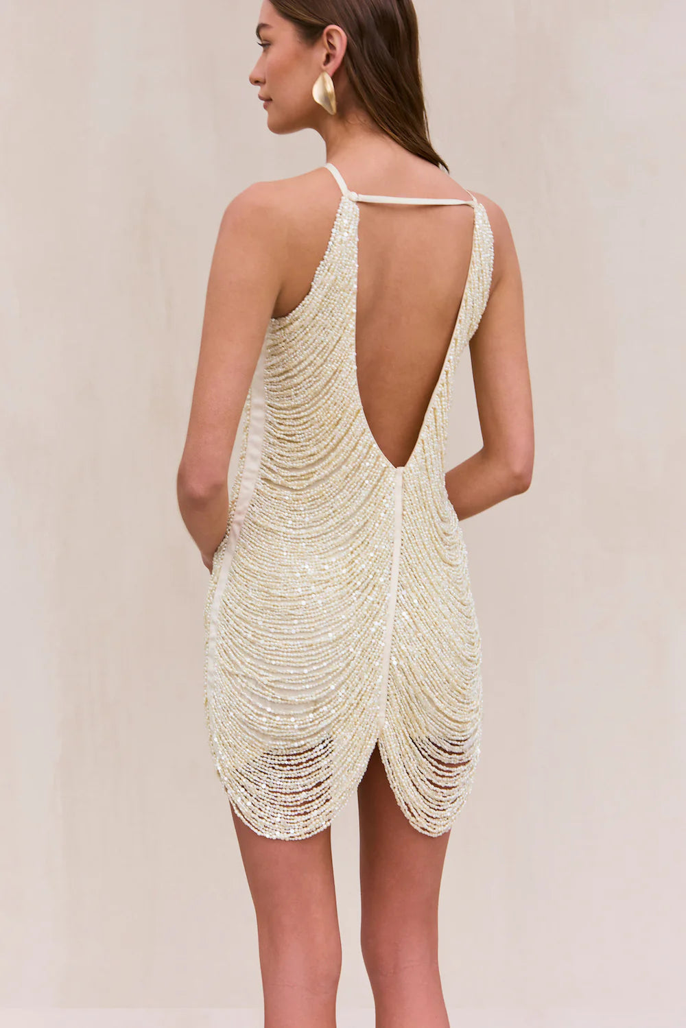 Indulge in the luxurious and exclusive Domina Dress by Cult Gaia. This exquisite halter dress boasts a layered and draped faux pearl fringe that gracefully moves with you. The plunging open back and flattering v-cut silhouette make this mini dress a must-have for any elegant occasion. Elevate your style with this captivating piece.