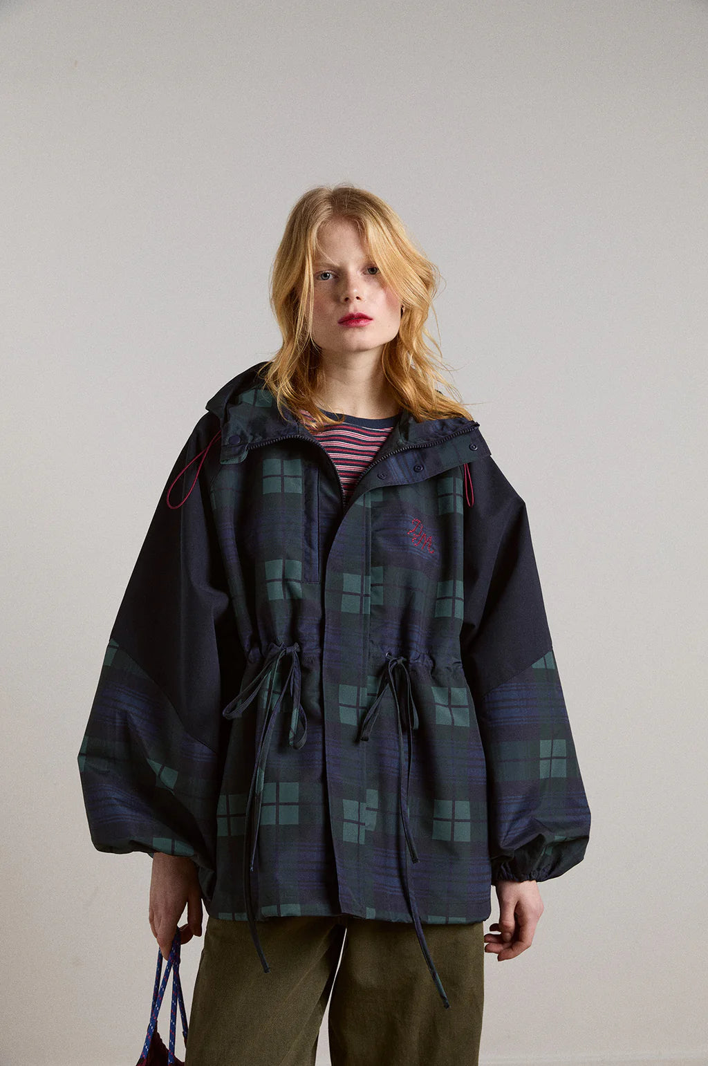 Embrace rainy days with the Liu Coat from Damson Madder, featuring a classic Black Watch tartan design crafted from shower-resistant fabric. Its balloon-style cuffs, adjustable hood, and cinchable waist offer both comfort and a flattering silhouette, while signature 'DM' embroidery adds a touch of distinction. Equipped with practical pockets and thoughtful details, this coat effortlessly combines style and functionality, making it the perfect shield against wet weather.