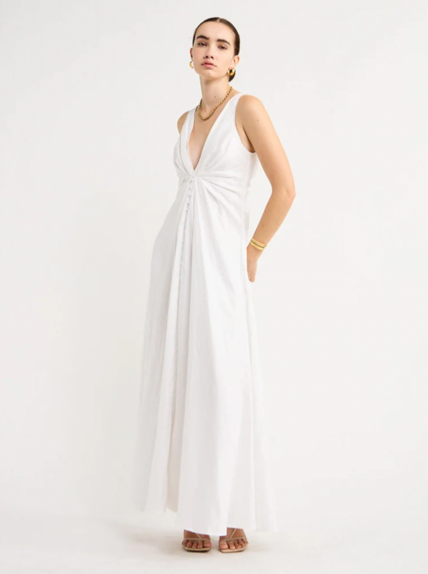 Adorn yourself with the elegance of the Sabrina Linen Maxi Dress in White. Crafted from Flax Linen fabrication for a relaxed easy fit, this maxi dress features a plunging neckline, a gathered twist front feature, functional linen-covered buttons, and a V-line open back with spaghetti tie fastening. With a graceful full skirt, this dress will be your go-to choice for summer getaways, birthday celebrations and refined holiday dressing.