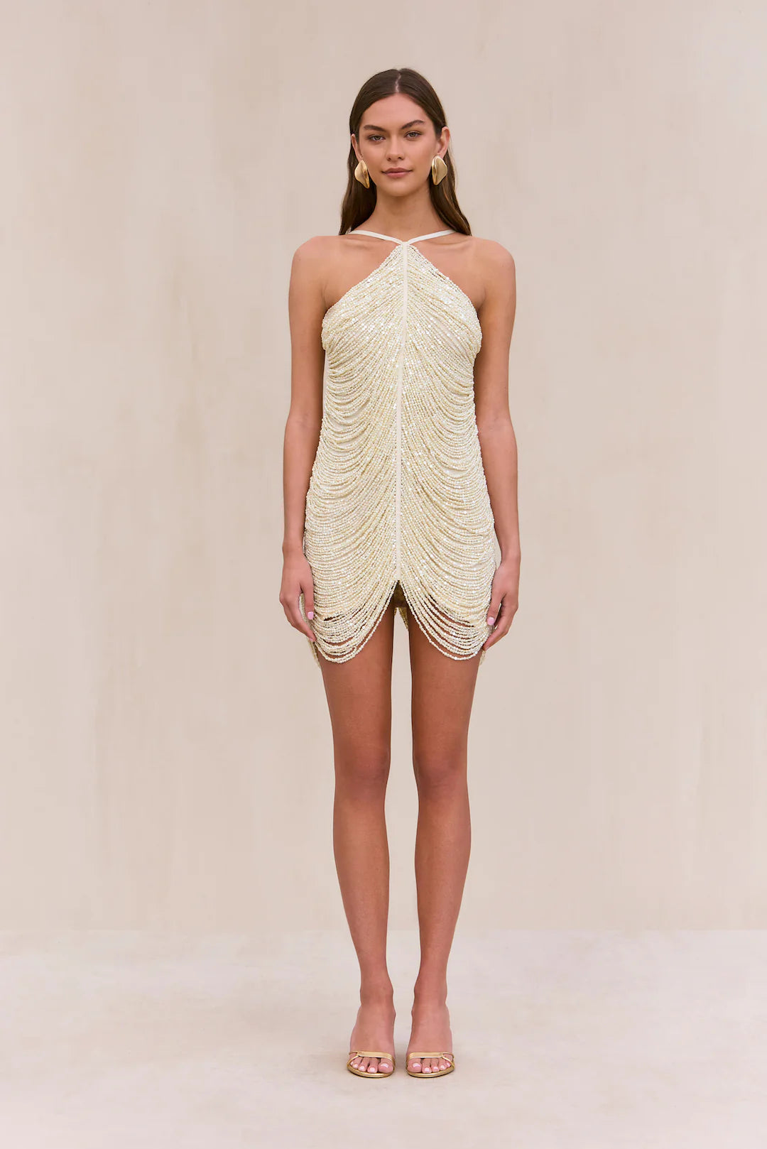 Indulge in the luxurious and exclusive Domina Dress by Cult Gaia. This exquisite halter dress boasts a layered and draped faux pearl fringe that gracefully moves with you. The plunging open back and flattering v-cut silhouette make this mini dress a must-have for any elegant occasion. Elevate your style with this captivating piece.