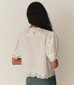 Load image into Gallery viewer, Crafted from lightweight, crisp ramie, the Idella Top from Doen features a plunging V-neckline, short puffed sleeves, and intricate embroidered lace details. Mother-of-pearl buttons adorn the front, while lace insets add delicate touches. This antique-inspired top is perfect for a breezy, feminine look.
