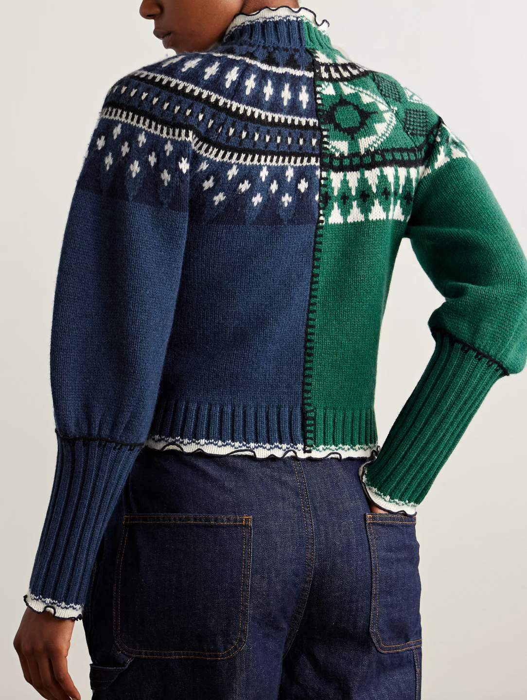 Sea's Linea cardigan masterfully blends two distinct aesthetics into one captivating piece. Crafted from sumptuous merino wool, this intarsia-knit design features Fair Isle-inspired motifs that create visual intrigue, while delicate ruffled trims add an unexpected feminine touch. The clever split construction gives the illusion of contrasting styles sewn together, making it a conversation-starting layer that transforms any basic turtleneck into an effortlessly sophisticated ensemble. 