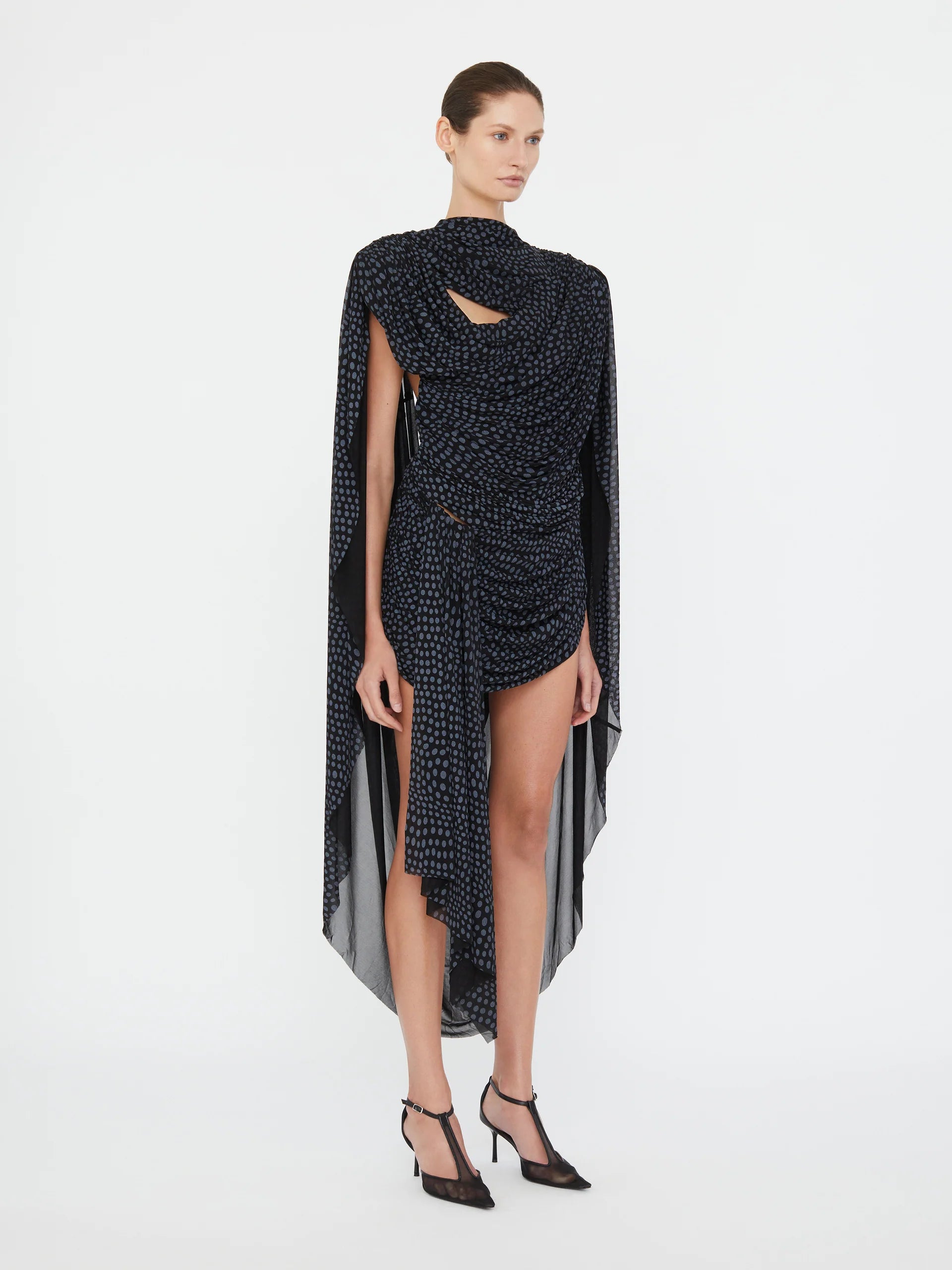 Embrace a nostalgic 90s vibe with the Torrent Draped Mini Dress by Christopher Esber, featuring a striking blue on black warped polka dot pattern inspired by a summer rain shower. The mini silhouette, enriched with gathered and cinched drapes, creates dynamic movement and captivating dimension. Its asymmetric draped skirt and fully lined construction offer effortless style and comfort, making it the perfect choice for standing out with subtle, artistic flair. 