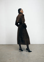 Load image into Gallery viewer, Elevate your wardrobe with the Brown Suede Trench Coat from Desavary London. Crafted with luxurious suede, this double breasted coat boasts an oversized fit and structured shoulders for a look that exudes sophistication. The buckle waist belt and storm flap add practicality to this statement piece. A must-have for any fashion-forward individual.
