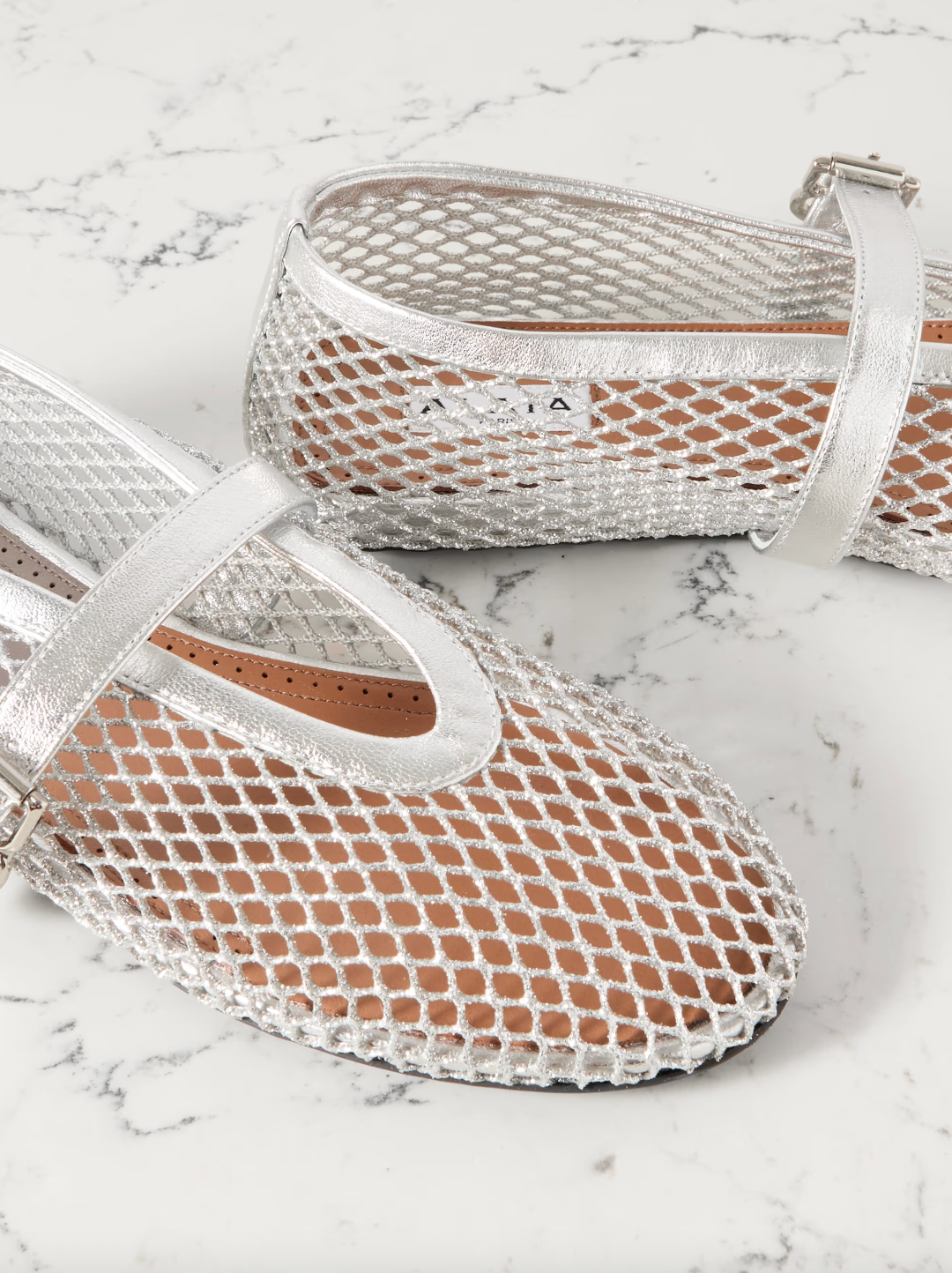 Elevate your wardrobe with Alaïa's modern take on the classic ballet flat. Crafted in Italy from silver mesh and metallic leather straps, these flats add a touch of glamour to any ensemble. With their comfortable round toes, they're perfect for everyday wear.