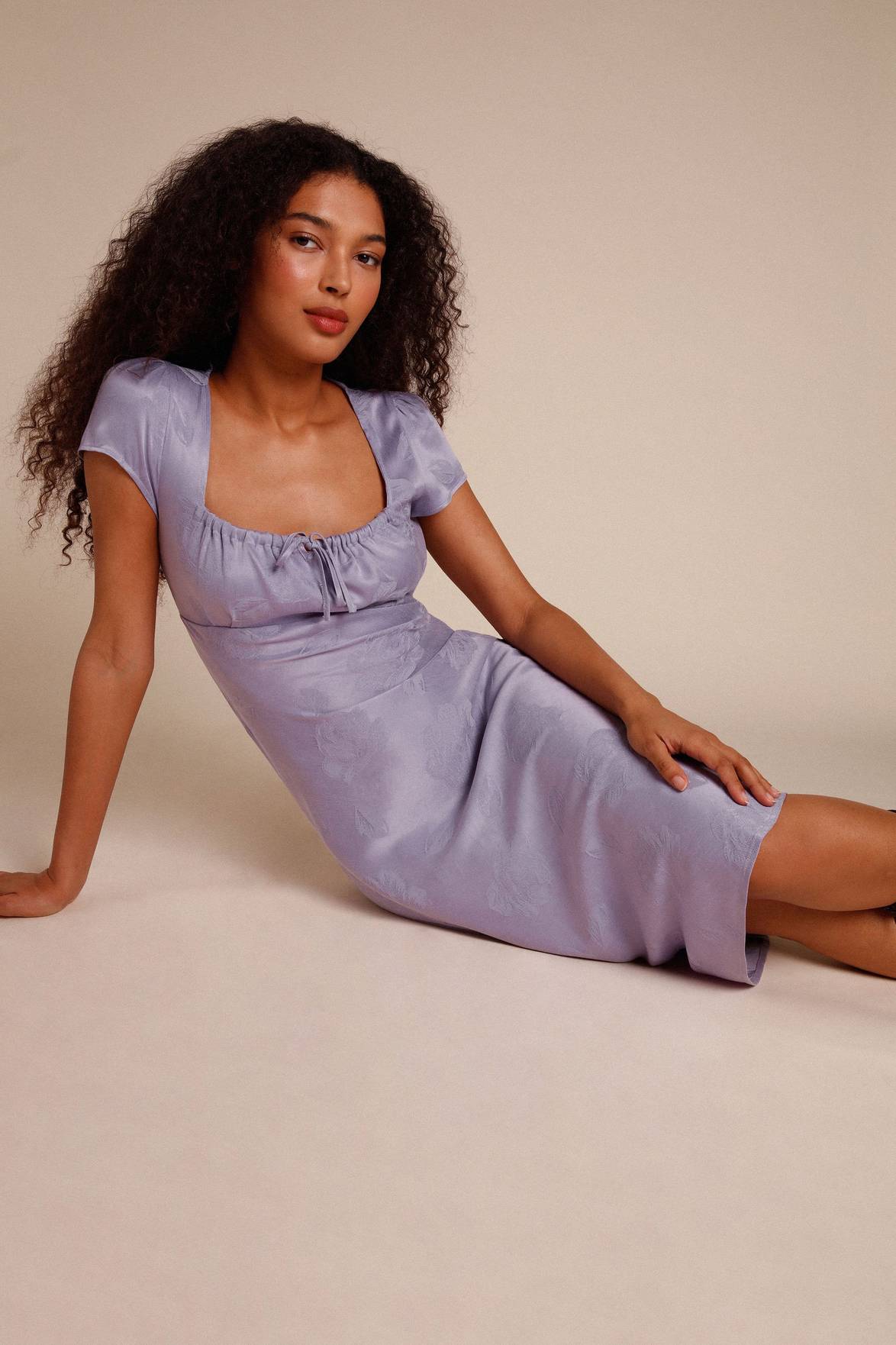 Introducing the versatile Robe Ines. This midi dress features a flattering gathered design on the chest with a unique knot detail. Its bias cut adds a touch of elegance, while the side zipper ensures a perfect fit. Available in lilac jacquard, this dress is the perfect addition to your wardrobe.