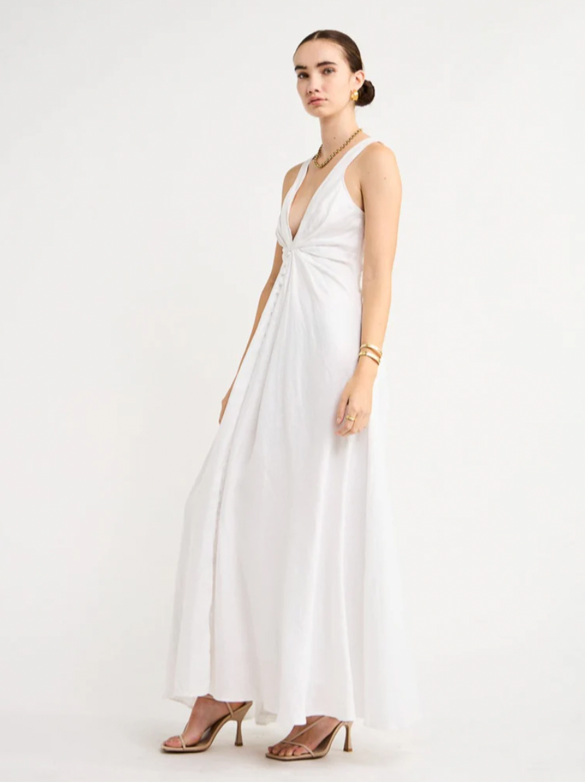 Adorn yourself with the elegance of the Sabrina Linen Maxi Dress in White. Crafted from Flax Linen fabrication for a relaxed easy fit, this maxi dress features a plunging neckline, a gathered twist front feature, functional linen-covered buttons, and a V-line open back with spaghetti tie fastening. With a graceful full skirt, this dress will be your go-to choice for summer getaways, birthday celebrations and refined holiday dressing.