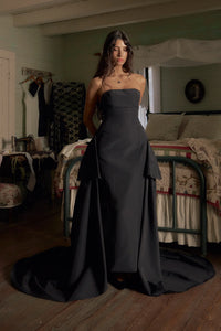 Be the life of the party in our Funny Face Gown Noir. Strapless column gown accentuates curves with built-in corset and hip padding. Side bustles and back peplum add playful flair. Functional buttons and invisible zipper down center back. Be the talk of the town in this daring and stylish gown!