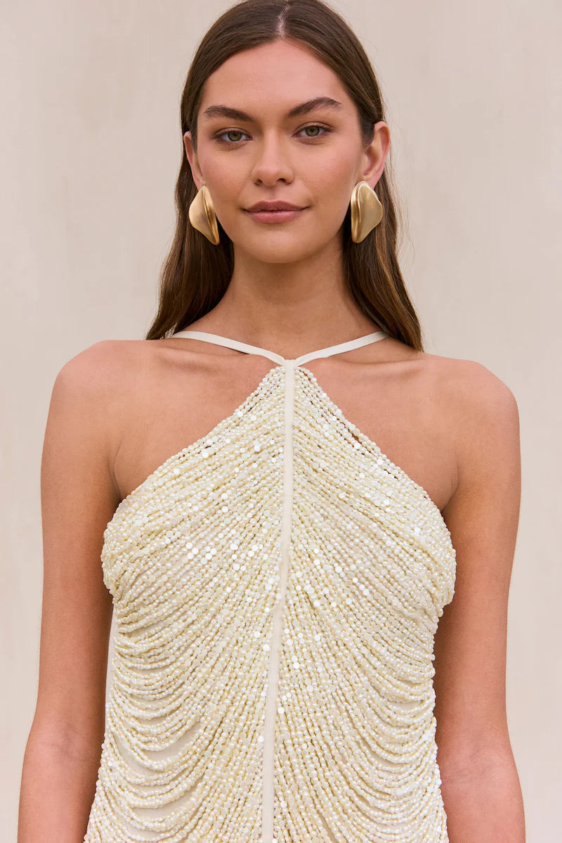 Indulge in the luxurious and exclusive Domina Dress by Cult Gaia. This exquisite halter dress boasts a layered and draped faux pearl fringe that gracefully moves with you. The plunging open back and flattering v-cut silhouette make this mini dress a must-have for any elegant occasion. Elevate your style with this captivating piece.