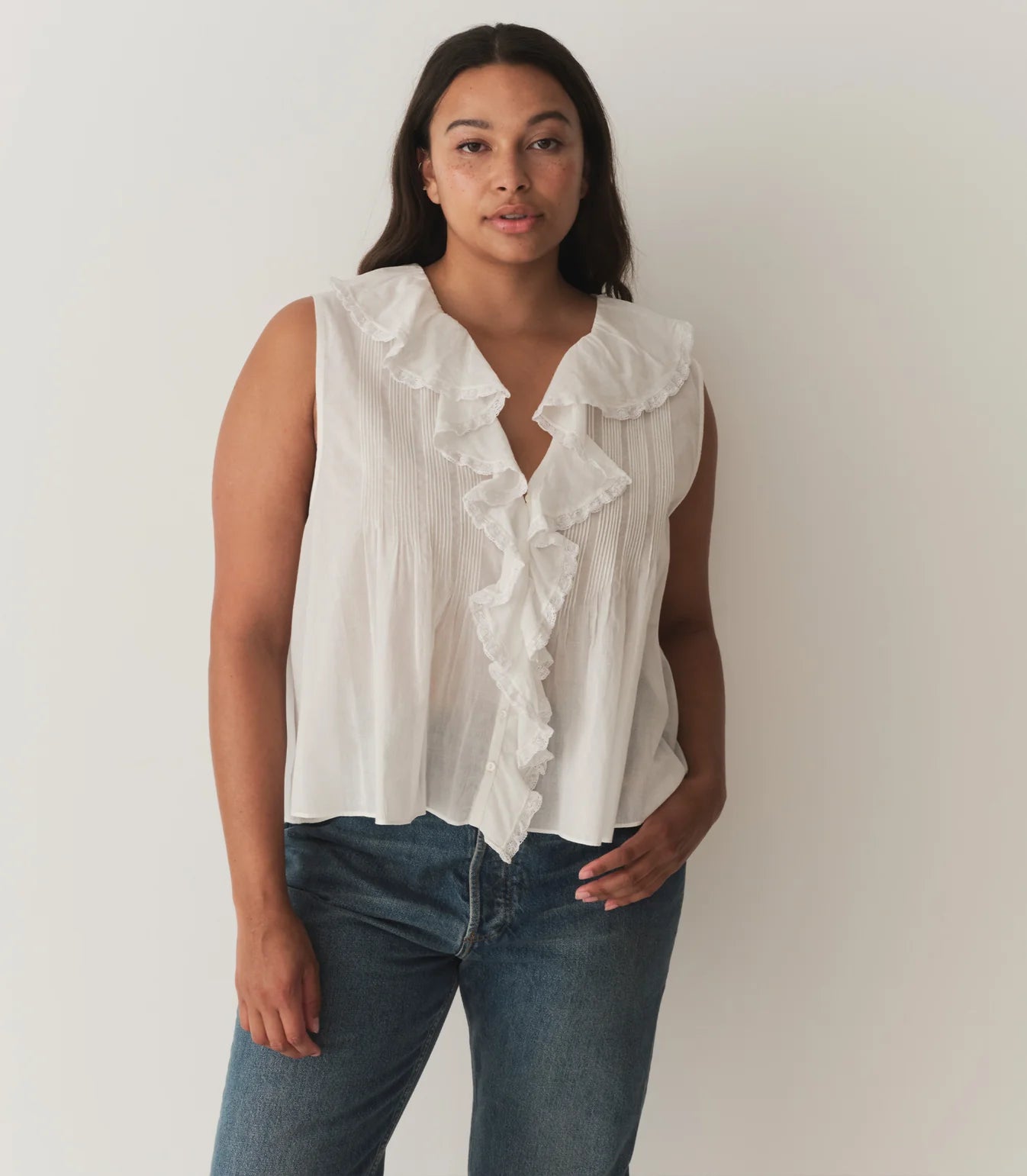 Indulge in the elegance of DOEN's Hilda Top. Made from organic cotton, this white voile top features a concealed front button fastening and delicate lace trim. Plisse details and a ruffle collar add a touch of sophistication. Perfect for a luxurious and stylish look