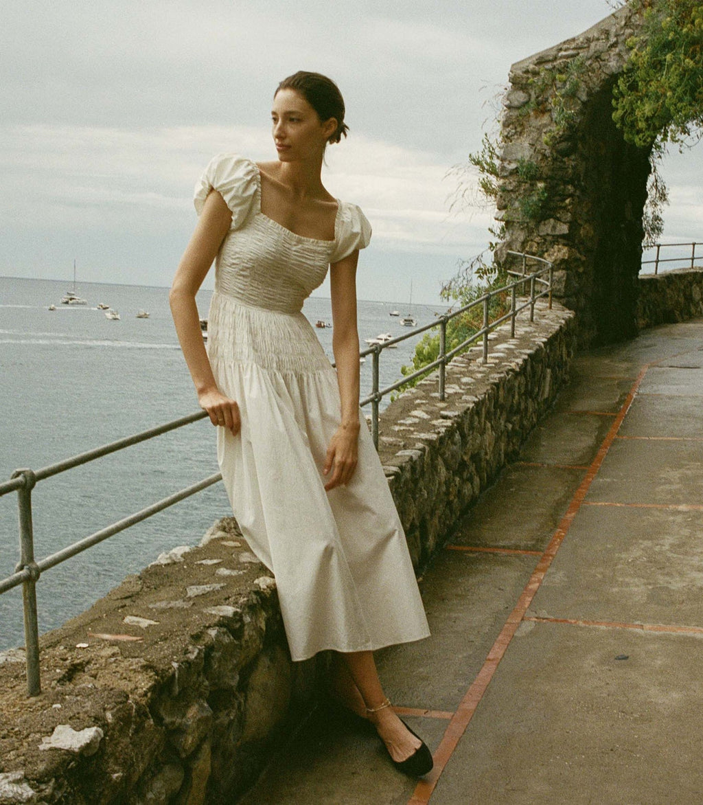 In a crisp cotton poplin, the Katherina—which draws inspiration from our bestselling Pamelina Dress and is a favorite of our co-founder Katherine—features short puffed sleeves and a square neckline trimmed with petite ruffles. A shirred bodice with elasticated smocking at the back gives way to an ankle-length skirt.