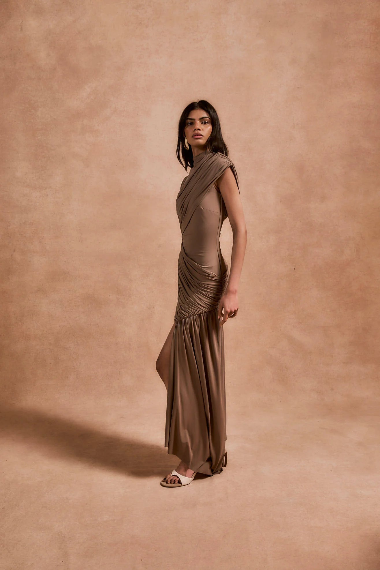 The Ravenna Mini Dress in Taupe offers a graceful silhouette with its asymmetrical high-low hemline and ruched detailing. Designed to fit true to size, this sleeveless, form-fitting dress effortlessly enhances your natural shape, making it ideal for special events. Its elegant taupe color pairs beautifully with gold or silver jewelry and classic pumps, ensuring a polished and confident look every time.