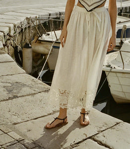 In crisp organic cotton poplin, the antique-inspired DÔEN Heirloom Gloriane Skirt features a high waist with a fixed tie and a full, A-line silhouette. Floral embroidery with hand-done cutwork adorns the hem, which falls to just above the ankle, while an invisible zipper and hook-and-eye closure fastens at the side.