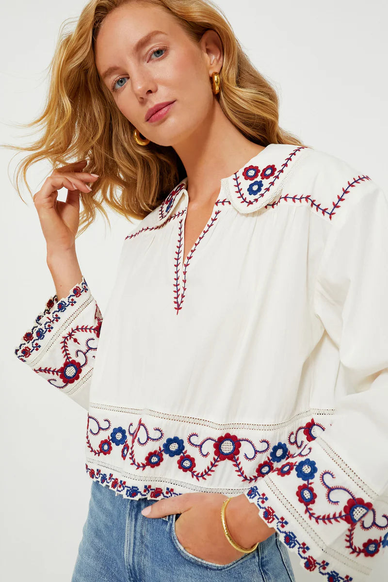 The Soren Embroidery Long Sleeve Top from Sea New York combines effortless style with sophisticated details. Crafted from soft cotton, this blouse features a collared V-neckline and long bell sleeves with subtle shoulder pleats for a refined silhouette. Elegant contrast embroidery adorns the hem and cuffs, adding a delicate, feminine touch. Versatile and modern, it pairs seamlessly with denim and flats for an easy yet polished look that channels boho-chic cool with understated elegance.