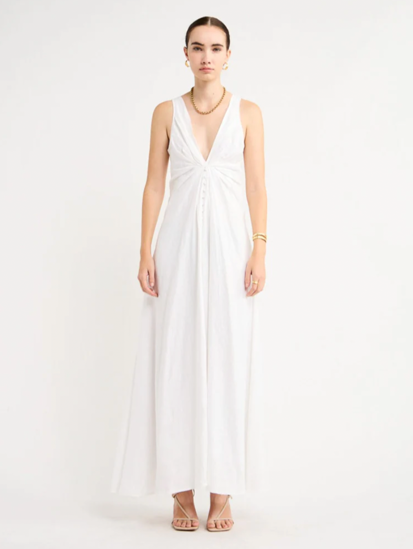 Adorn yourself with the elegance of the Sabrina Linen Maxi Dress in White. Crafted from Flax Linen fabrication for a relaxed easy fit, this maxi dress features a plunging neckline, a gathered twist front feature, functional linen-covered buttons, and a V-line open back with spaghetti tie fastening. With a graceful full skirt, this dress will be your go-to choice for summer getaways, birthday celebrations and refined holiday dressing.