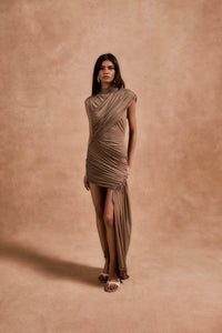 The Ravenna Mini Dress in Taupe offers a graceful silhouette with its asymmetrical high-low hemline and ruched detailing. Designed to fit true to size, this sleeveless, form-fitting dress effortlessly enhances your natural shape, making it ideal for special events. Its elegant taupe color pairs beautifully with gold or silver jewelry and classic pumps, ensuring a polished and confident look every time.
