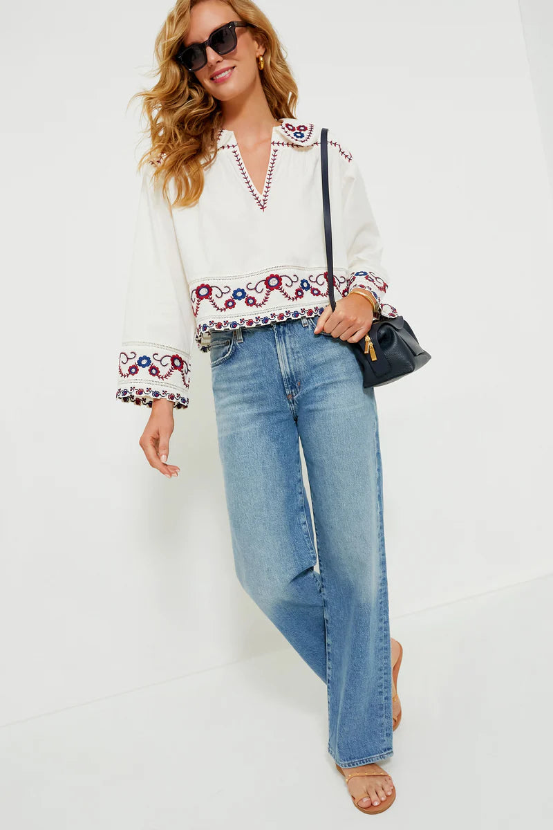 The Soren Embroidery Long Sleeve Top from Sea New York combines effortless style with sophisticated details. Crafted from soft cotton, this blouse features a collared V-neckline and long bell sleeves with subtle shoulder pleats for a refined silhouette. Elegant contrast embroidery adorns the hem and cuffs, adding a delicate, feminine touch. Versatile and modern, it pairs seamlessly with denim and flats for an easy yet polished look that channels boho-chic cool with understated elegance.