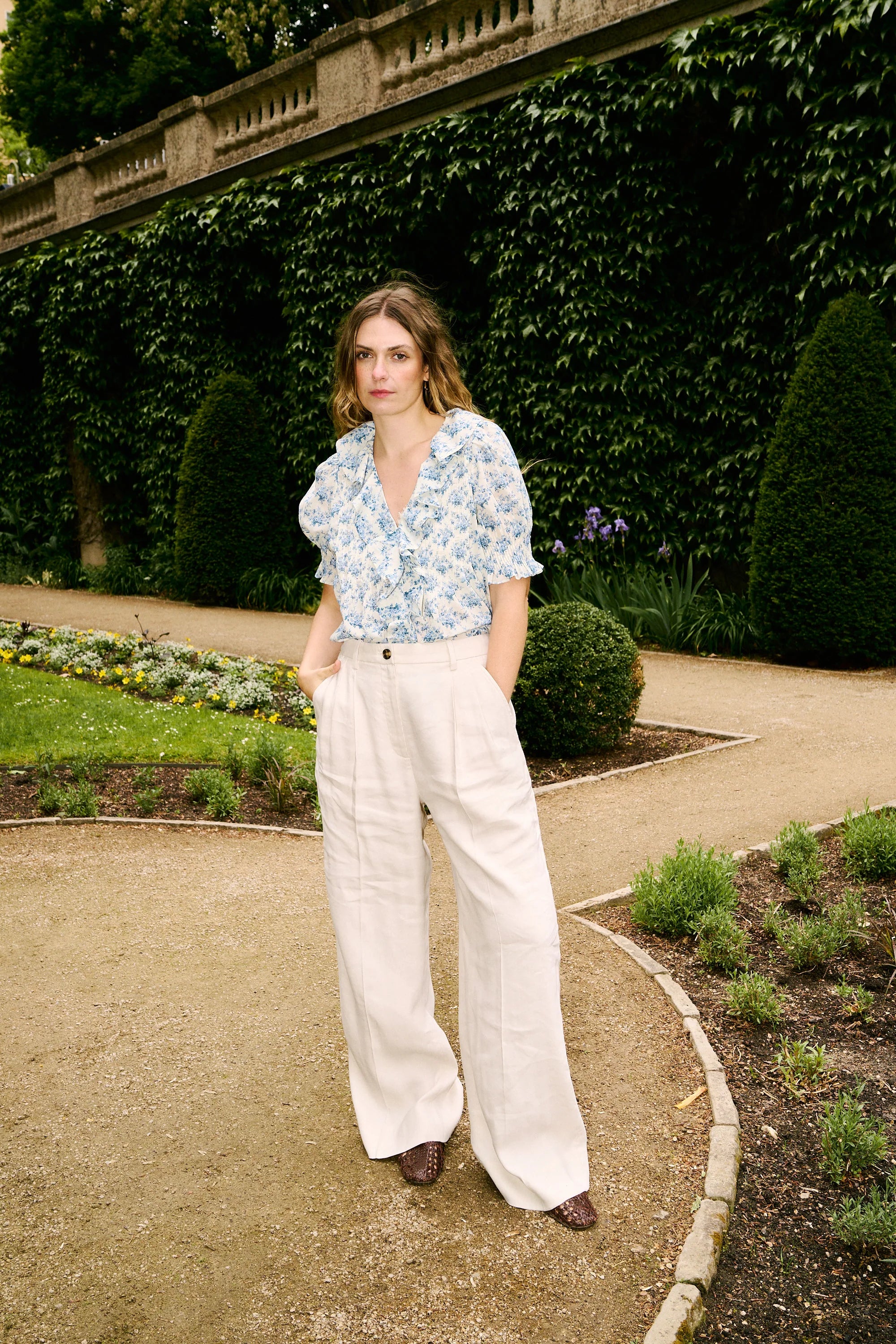 The Henri Top is a stunning blend of romantic Victorian aesthetics and modern sophistication. Made from soft, lightweight organic cotton voile, it features a plunging V-neckline adorned with cascading lace-trimmed ruffles. Delicate clustered pintucks accent the yoke and puffed sleeves, while hidden starburst buttons add a unique touch. Perfect for both casual outings and special occasions, this blouse effortlessly elevates any outfit with its vintage charm and playful elegance.
