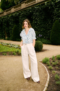The Henri Top is a stunning blend of romantic Victorian aesthetics and modern sophistication. Made from soft, lightweight organic cotton voile, it features a plunging V-neckline adorned with cascading lace-trimmed ruffles. Delicate clustered pintucks accent the yoke and puffed sleeves, while hidden starburst buttons add a unique touch. Perfect for both casual outings and special occasions, this blouse effortlessly elevates any outfit with its vintage charm and playful elegance.
