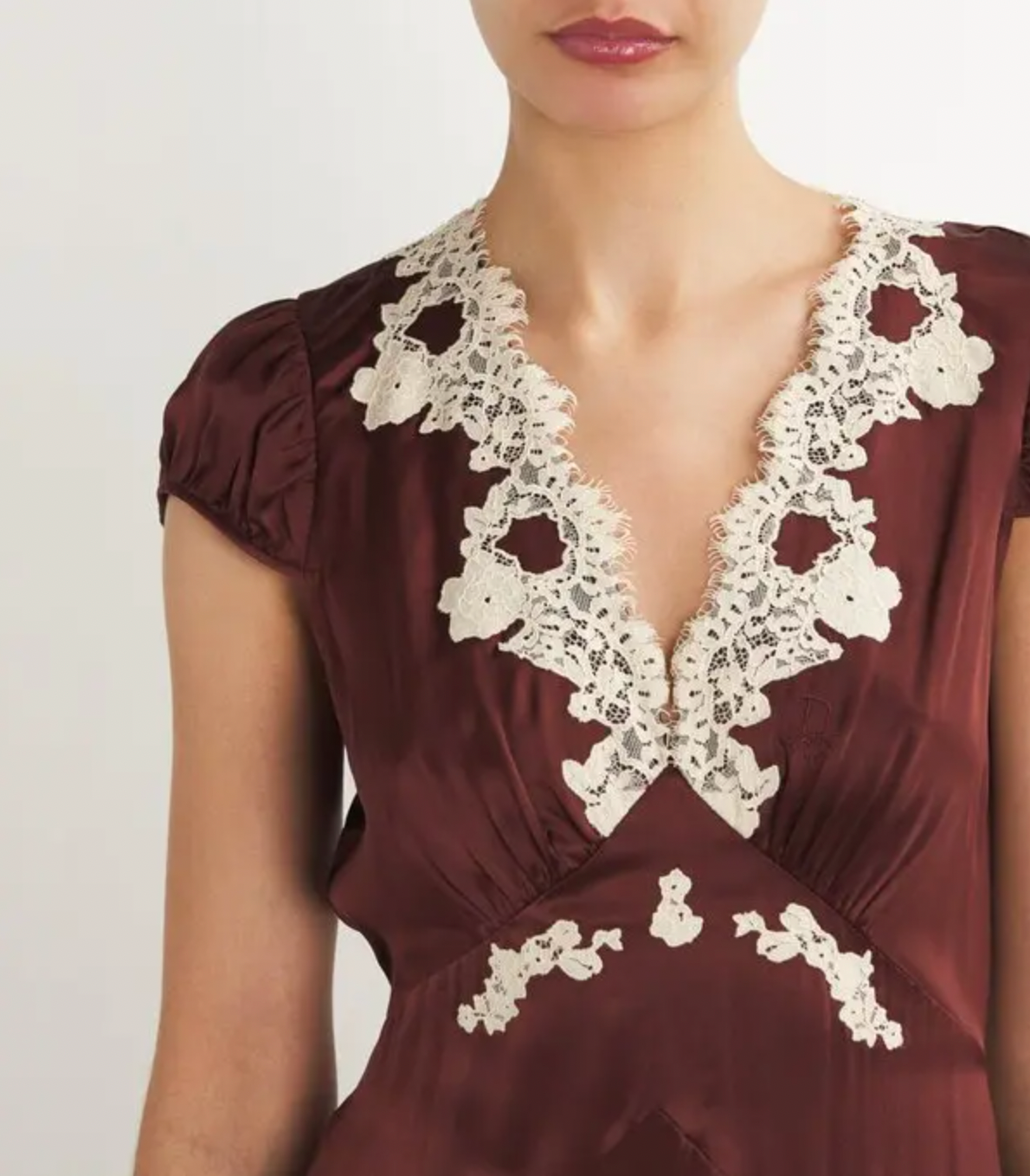 The Silk Lace-Trim Coraline Midi Dress channels the refined elegance of the 1930s with expertly crafted details. Made from lush silk satin, it gracefully drapes the body, enhanced by whimsical gathered cap sleeves. The plunging V-neckline highlights delicate embroidered scallop lace, while the fitted bodice transitions into a flattering bias-cut midi skirt. Adjustable back ties offer a personalized fit, and a subtle embroidered “D” on the bust adds a distinctive signature touch. 