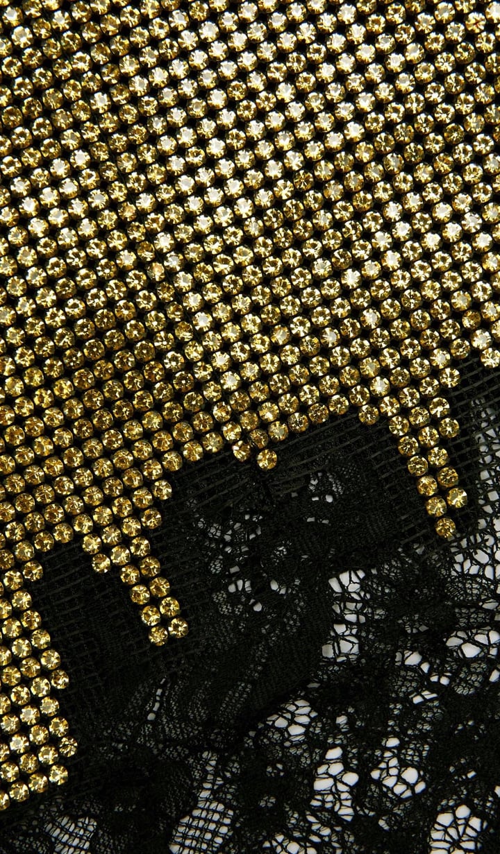 Elevate your evening wardrobe with the Champagne Crystal Set—a dazzling combination of a relaxed-fit chainmail top and a flirtatious mini skirt. The top features champagne crystals, lace-trimmed hem, button-back closure, and full lining for comfort and polish. The matching fitted mini skirt, detailed with delicate lace trim and a back zipper, offers subtle allure with its minimal stretch and unlined finish. 