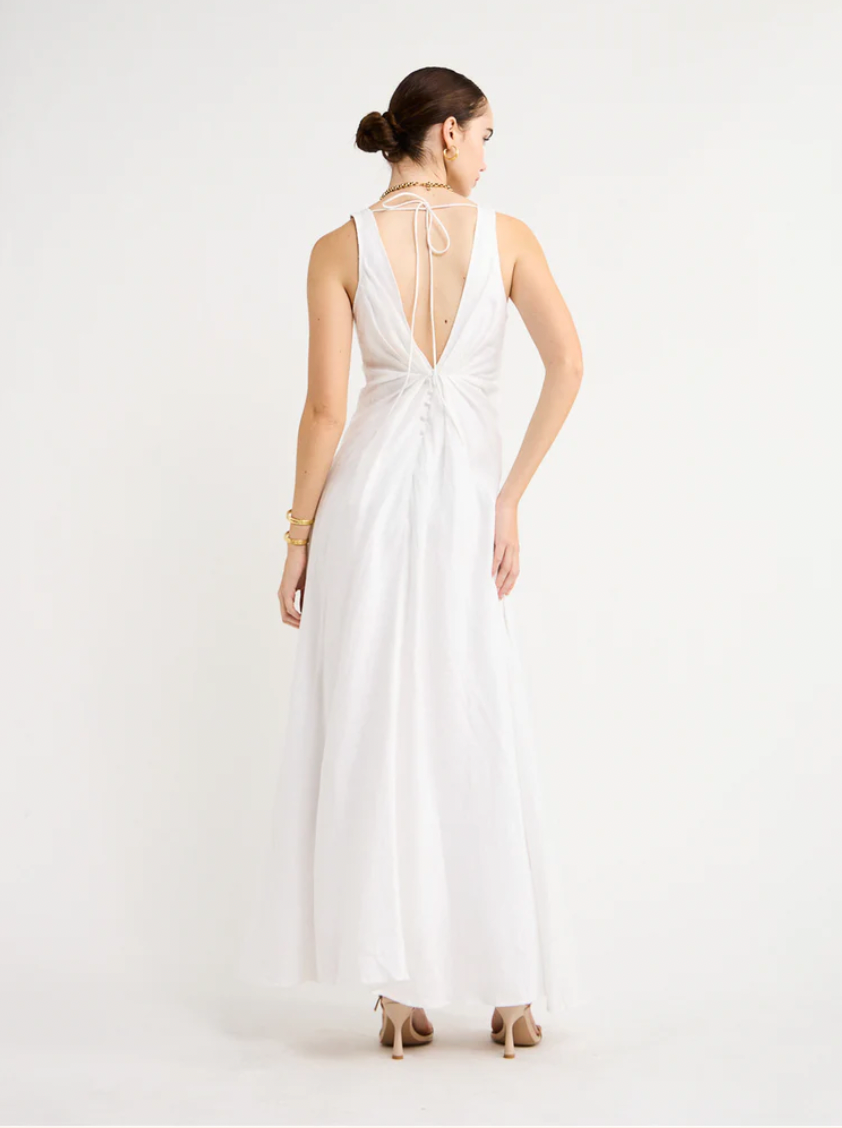 Adorn yourself with the elegance of the Sabrina Linen Maxi Dress in White. Crafted from Flax Linen fabrication for a relaxed easy fit, this maxi dress features a plunging neckline, a gathered twist front feature, functional linen-covered buttons, and a V-line open back with spaghetti tie fastening. With a graceful full skirt, this dress will be your go-to choice for summer getaways, birthday celebrations and refined holiday dressing.