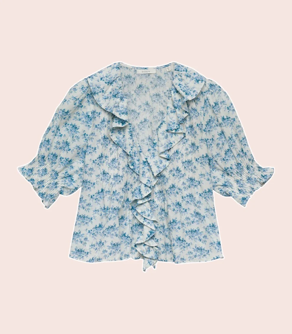 The Henri Top is a stunning blend of romantic Victorian aesthetics and modern sophistication. Made from soft, lightweight organic cotton voile, it features a plunging V-neckline adorned with cascading lace-trimmed ruffles. Delicate clustered pintucks accent the yoke and puffed sleeves, while hidden starburst buttons add a unique touch. Perfect for both casual outings and special occasions, this blouse effortlessly elevates any outfit with its vintage charm and playful elegance.