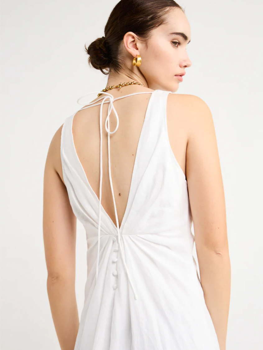 Adorn yourself with the elegance of the Sabrina Linen Maxi Dress in White. Crafted from Flax Linen fabrication for a relaxed easy fit, this maxi dress features a plunging neckline, a gathered twist front feature, functional linen-covered buttons, and a V-line open back with spaghetti tie fastening. With a graceful full skirt, this dress will be your go-to choice for summer getaways, birthday celebrations and refined holiday dressing.