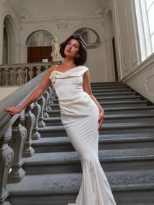 Elevate your elegance with the Celine Corset Gown, a luxurious satin masterpiece designed to flatter every figure. Featuring a corset waist that sculpts your silhouette and graceful draping at the hips, this gown enhances your natural curves. The asymmetric design highlights a delicate rosette on one shoulder and a flowing scarf on the other, adding a unique touch of sophistication. The slightly flared hemline completes this stunning look, perfect for making a memorable entrance at any special occasion.
