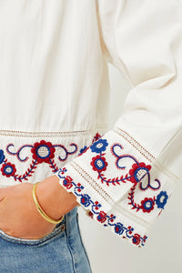 The Soren Embroidery Long Sleeve Top from Sea New York combines effortless style with sophisticated details. Crafted from soft cotton, this blouse features a collared V-neckline and long bell sleeves with subtle shoulder pleats for a refined silhouette. Elegant contrast embroidery adorns the hem and cuffs, adding a delicate, feminine touch. Versatile and modern, it pairs seamlessly with denim and flats for an easy yet polished look that channels boho-chic cool with understated elegance.