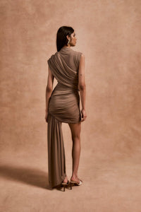 The Ravenna Mini Dress in Taupe offers a graceful silhouette with its asymmetrical high-low hemline and ruched detailing. Designed to fit true to size, this sleeveless, form-fitting dress effortlessly enhances your natural shape, making it ideal for special events. Its elegant taupe color pairs beautifully with gold or silver jewelry and classic pumps, ensuring a polished and confident look every time.