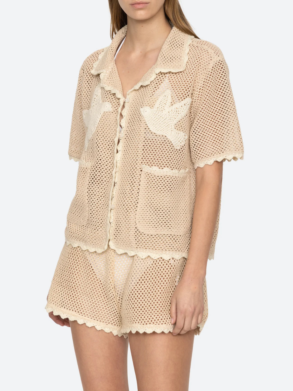 Upgrade your wardrobe with the Sally Crochet Shirt by SEA NY! This mid-weight, open knit shirt is designed for a slightly loose fit and is appliquéd with two delicate birds. Traced with scalloped trims, this beige and white crocheted cotton shirt is both stylish and comfortable. Button fastenings add a polished touch, making it perfect for any occasion.