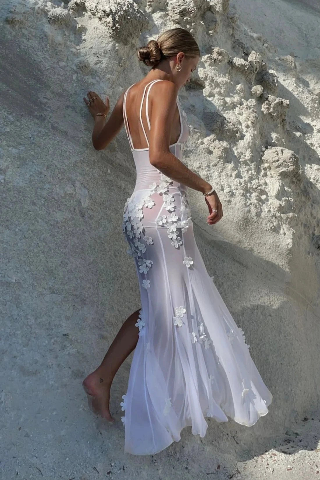 Indulge in luxury with the Daisy Maxi Dress. Hand-finished by skilled artisans, this white ruffle fairy dress features delicate 3-D flowers and mesh fabric for a perfect fit. The low neck, high slits, and double straps create an elegant hourglass silhouette, making it a versatile choice for a cover-up, maxi dress, or beach wedding attire.